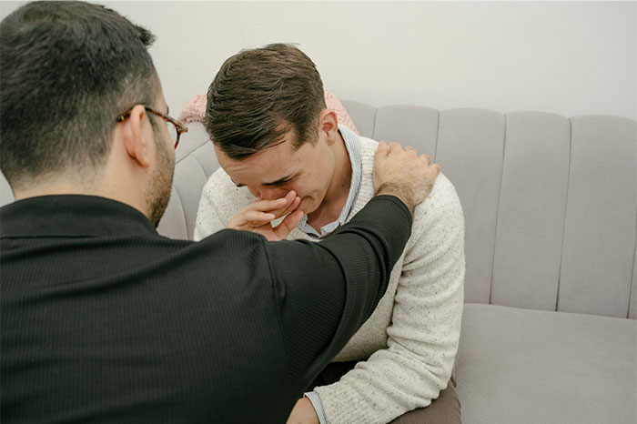 Man comforting another man showing emotional distress, highlighting the impact of pseudoscience and scams on mental health.