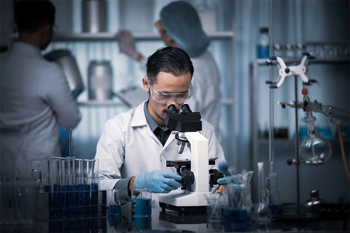 Scientist in a lab wearing protective gear, examining samples through a microscope, highlighting pseudoscience and scams.
