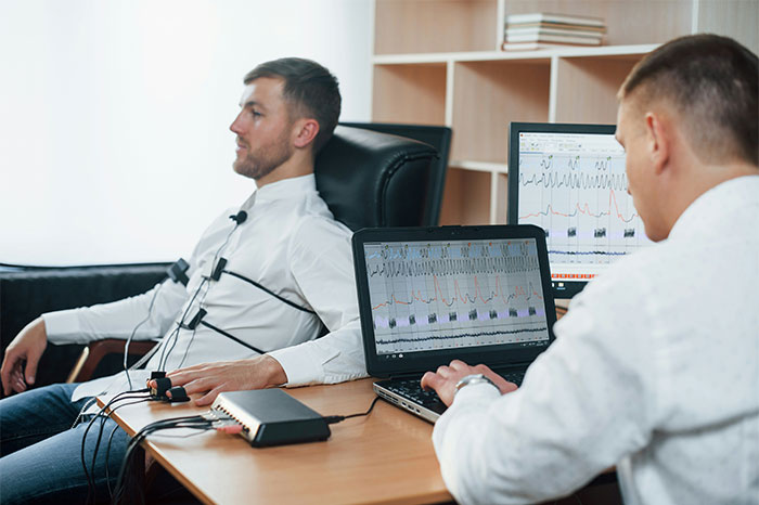 Man undergoing polygraph test with examiner monitoring charts on laptop, illustrating pseudoscience and scams.