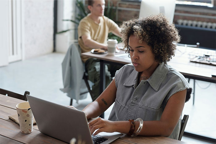 Woman working on laptop at a wooden desk in a casual office setting, highlighting pseudoscience and scams awareness.