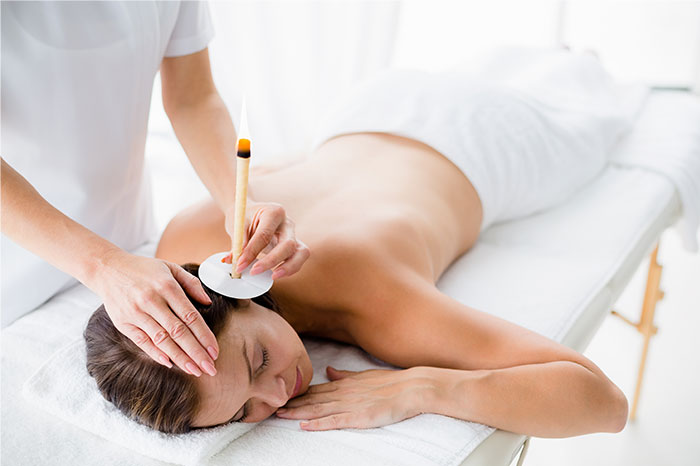 Woman lying on a massage table receiving an ear candling treatment, illustrating pseudoscience and scams in wellness.