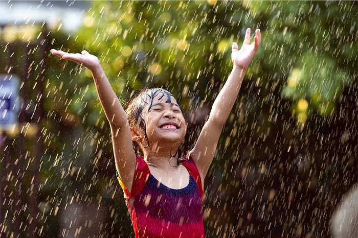 Young girl enjoying rain with arms raised, symbolizing joy and innocence amid pseudoscience and scam awareness.