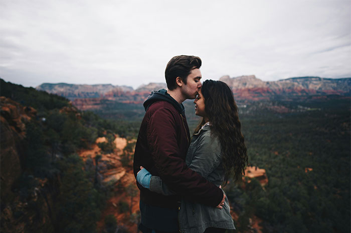 Couple embracing on a cliffside overlooking a forest and red rock formations, illustrating trust beyond pseudoscience and scams.