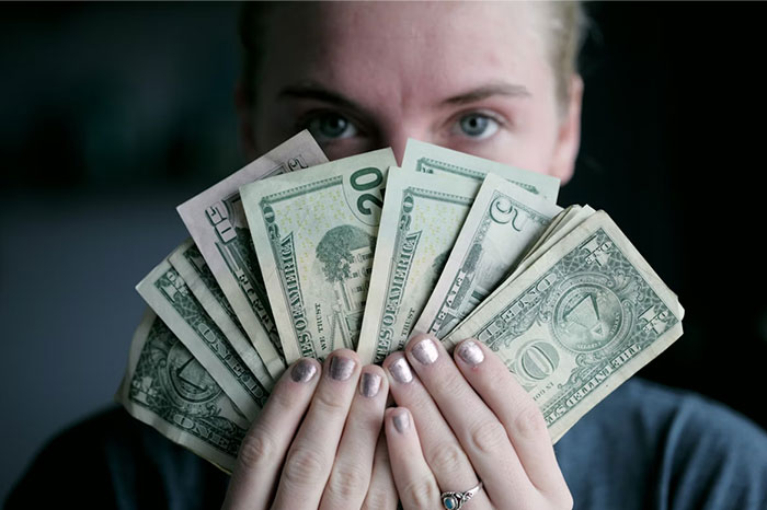 Person holding various US dollar bills close to their face, highlighting pseudoscience and scams related to money.
