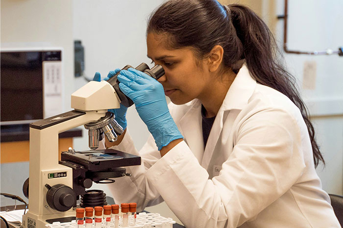 Scientist in lab coat examining samples using a microscope, illustrating pseudoscience and scam investigation concept.
