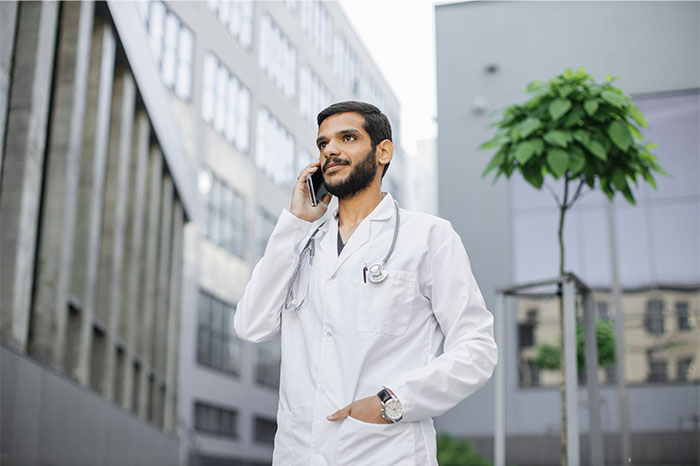Male doctor with stethoscope talking on phone outdoors, representing pseudoscience and scams in healthcare discussions.