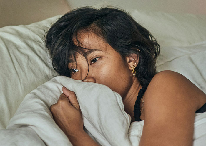 Woman lying in bed looking thoughtful, representing emotions related to things not mentioned until after marriage.