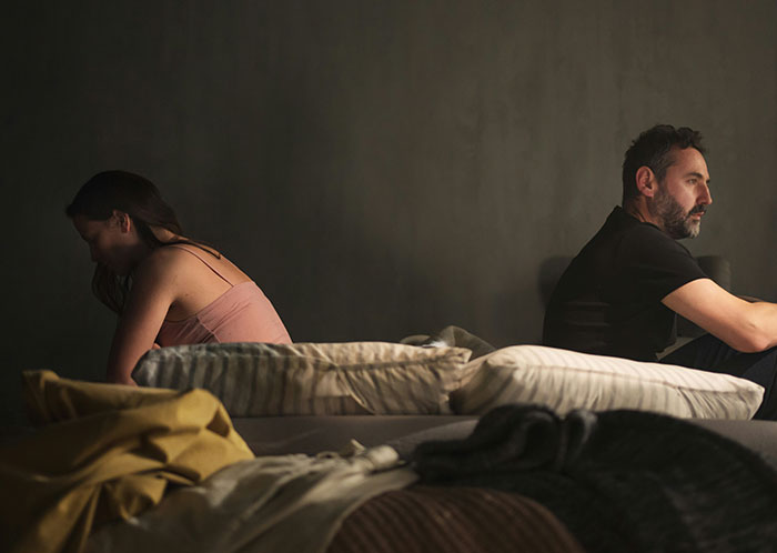 Couple sitting back to back on bed, showing tension and silence, illustrating things not mentioned after marriage.