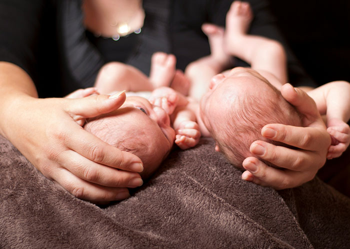 Two newborn babies resting on a soft blanket with hands gently supporting their heads after marriage changes.