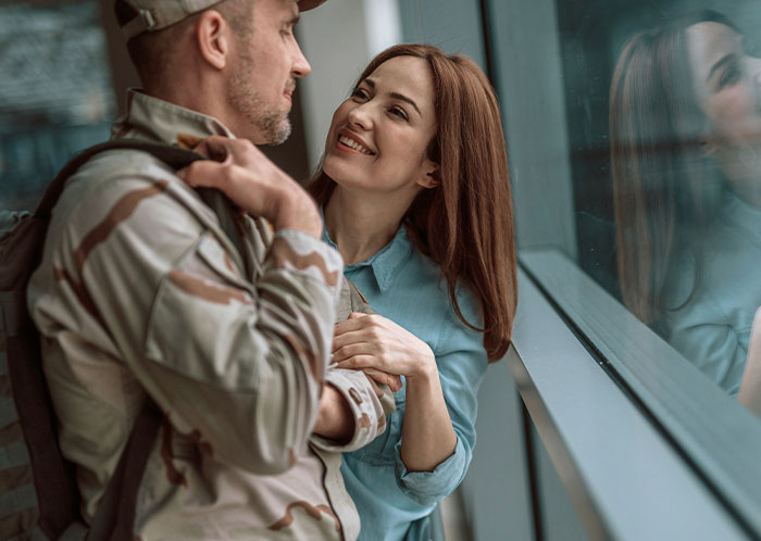 Woman smiling at man in military uniform by window, symbolizing things not mentioned until after marriage conversation.