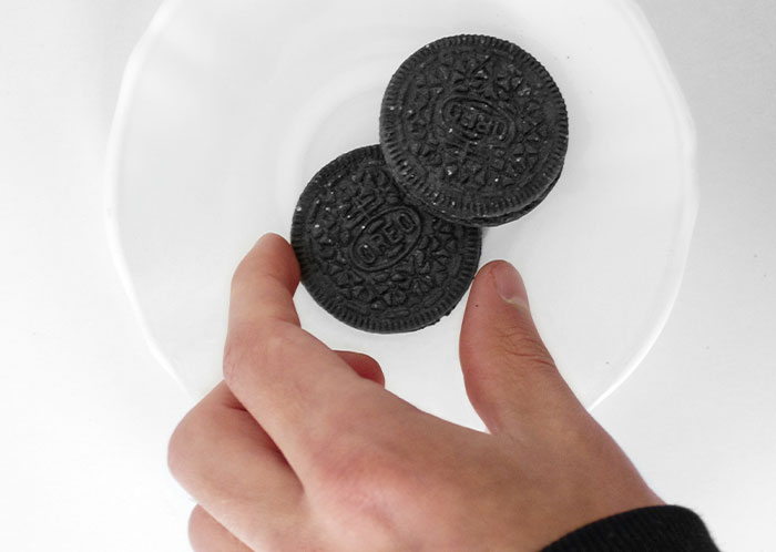 Hand holding Oreo cookies over a white plate representing things not mentioned until after marriage secrets.