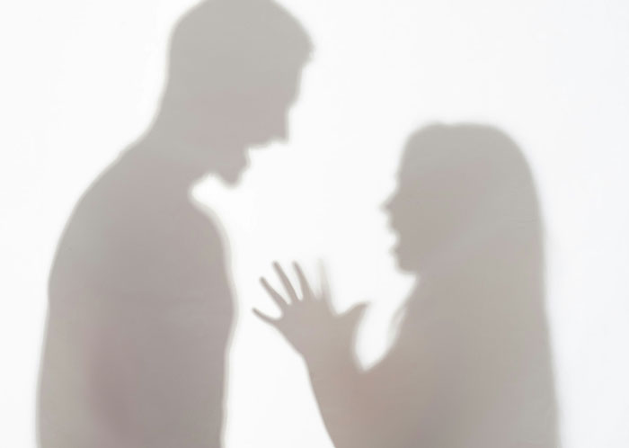 Silhouettes of a couple arguing with visible tension, representing things not mentioned until after marriage challenges.