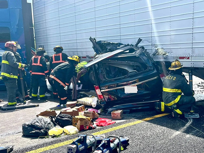 Firefighters attending to a crushed car after a truck driver made an illegal U-turn causing a fatal accident with three deaths.