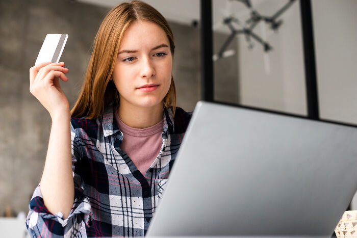 Young woman holding a credit card and using a laptop, focused on ticking big lifetime event online transaction.