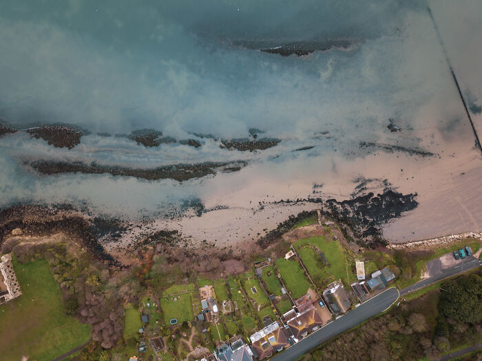 Aerial view of coastal shoreline with houses and gardens, illustrating ticking big lifetime event near water and land.