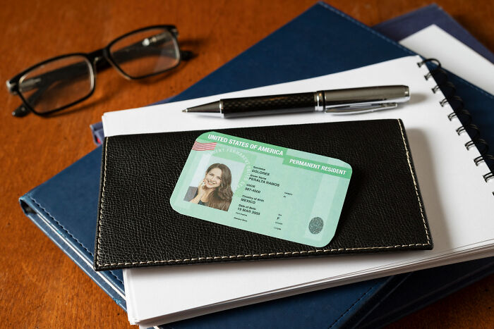 A permanent resident card on a leather wallet with pen, glasses, and notebooks, symbolizing ticking big lifetime event.