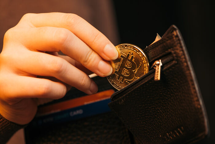 Hand placing a Bitcoin coin into a black leather wallet, symbolizing ticking big lifetime event in cryptocurrency investment.