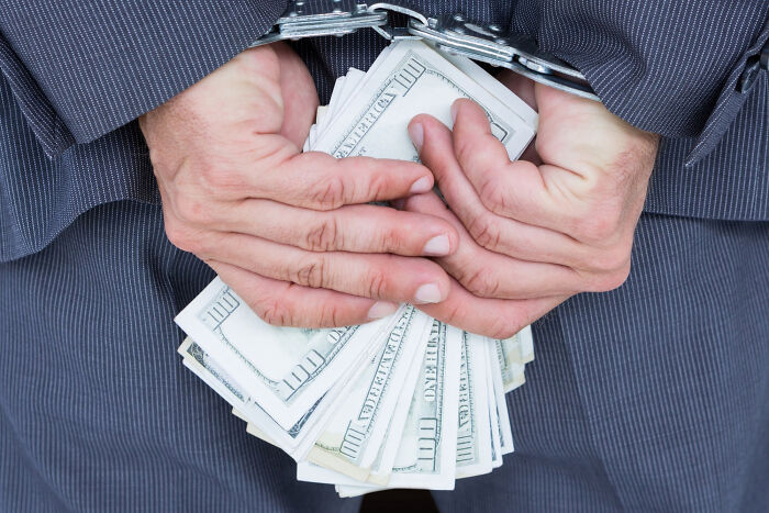 Person in handcuffs holding a large stack of cash, illustrating ticking big lifetime event financial risk.