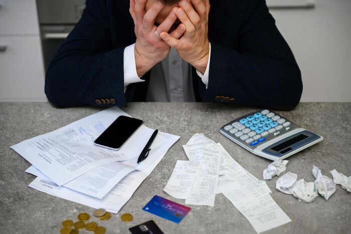 Person stressed over bills and receipts with calculator and credit cards, ticking big lifetime event financial moment.