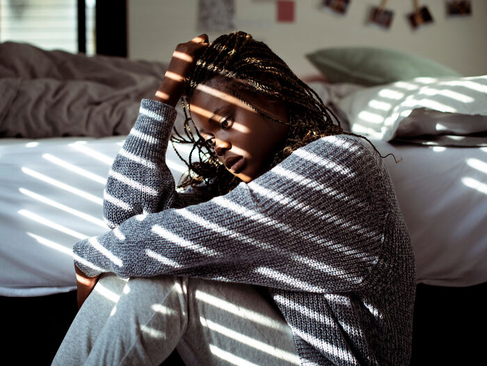 Woman sitting on floor in striped light and shadow, reflecting on ticking big lifetime event in a quiet room.