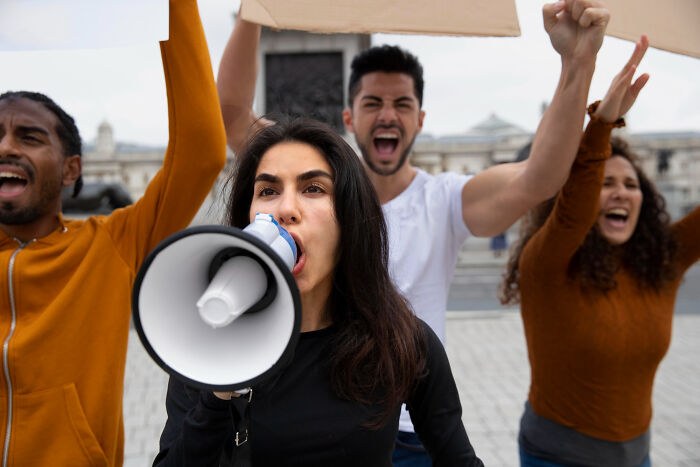 A group of young activists protesting outdoors with a woman using a megaphone, ticking big lifetime event message conveyed.