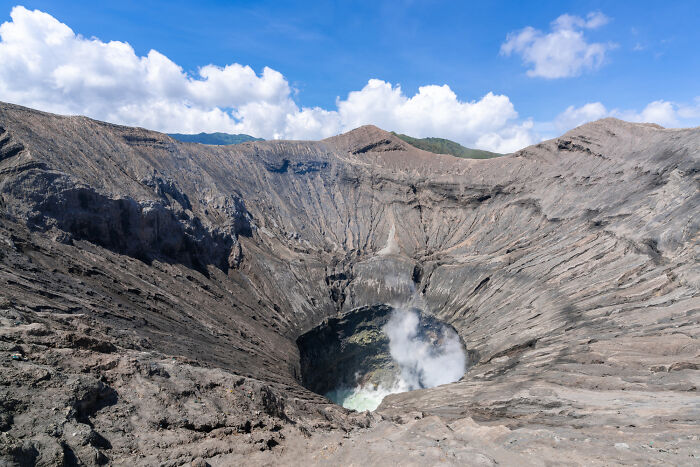 Volcanic crater emitting steam under blue sky, illustrating the ticking big lifetime event in nature's cycle.