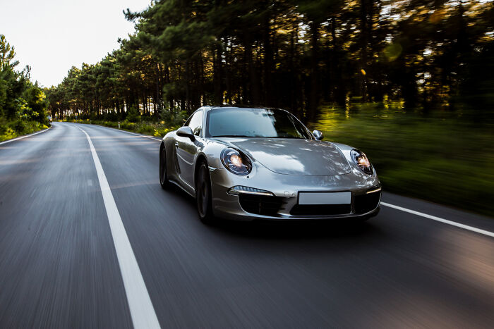 Silver sports car driving fast on a forest road, symbolizing ticking big lifetime event in motion and speed.