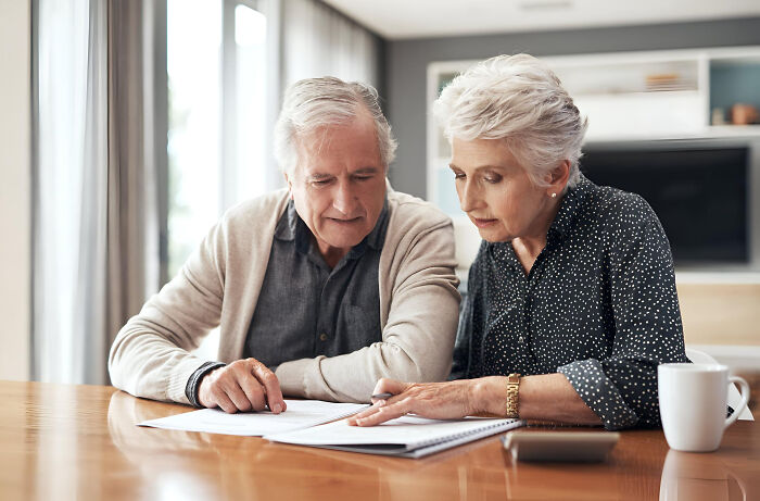 Older couple sitting at a table, reviewing documents together, symbolizing ticking big lifetime event planning.
