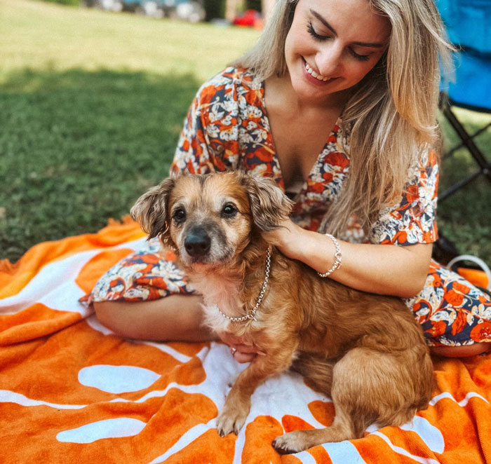 Tiki the timid rescue pup sitting on a blanket outdoors with a woman, finally feeling safe and loved.