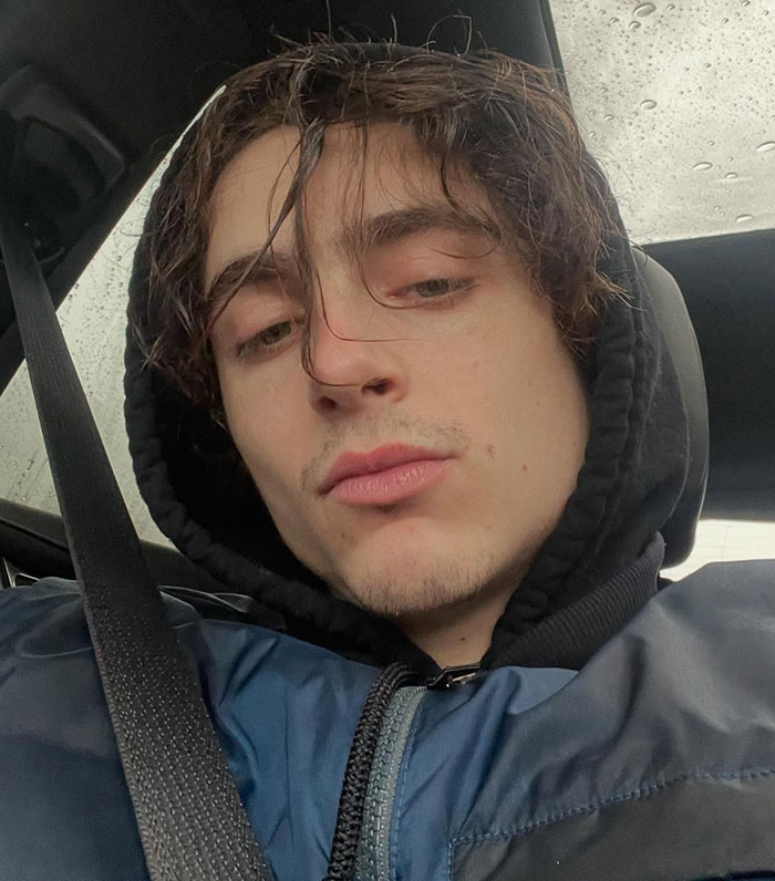 Timoth&eacute;e Chalamet in a car wearing a black hoodie and blue jacket, looking at the camera with a neutral expression.