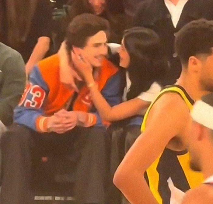 Kylie Jenner affectionately touching Timoth&eacute;e Chalamet while sitting courtside at a basketball game in casual attire.