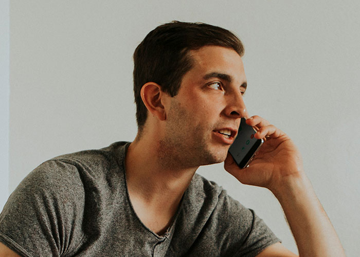 Man in gray shirt talking on phone, illustrating reaction related to woman appalled by dad’s response to dead grandchild birth. Man in gray shirt talking on phone, illustrating reaction related to woman appalled by dad’s response to dead grandchild birth.