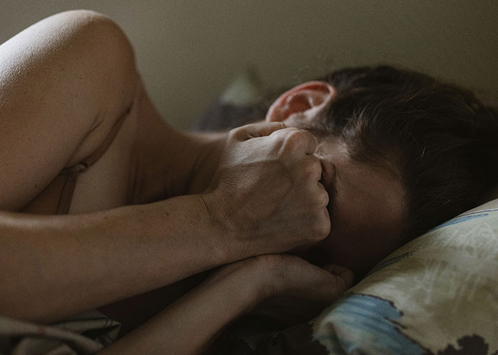 Woman lying in bed with face buried in hand, showing distress and appalled by dad’s reaction to dead grandchild news Woman lying in bed with face buried in hand, showing distress and appalled by dad’s reaction to dead grandchild news