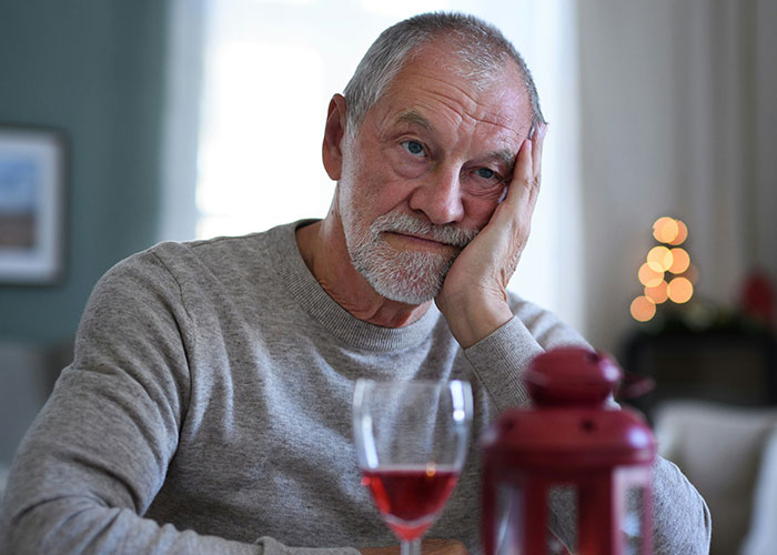 Elderly man looking appalled and contemplative sitting at a table with a glass of wine, reflecting on family matters. Elderly man looking appalled and contemplative sitting at a table with a glass of wine, reflecting on family matters.