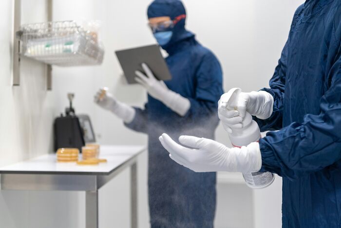 Scientists in protective suits spray disinfectant and document results in lab, highlighting tiny human mistakes impacting history.