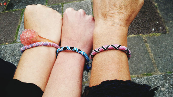 Three wrists wearing colorful handmade bracelets, illustrating common tourist traps and souvenir purchases outdoors.