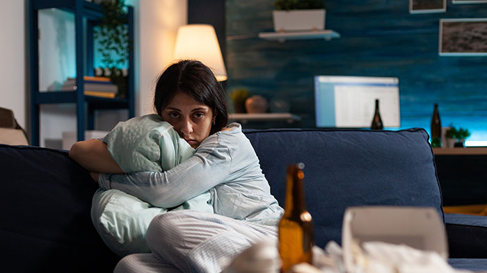 Young woman looking confused and upset on a couch after boyfriend&rsquo;s sister starts hitting on her in a tense living room.