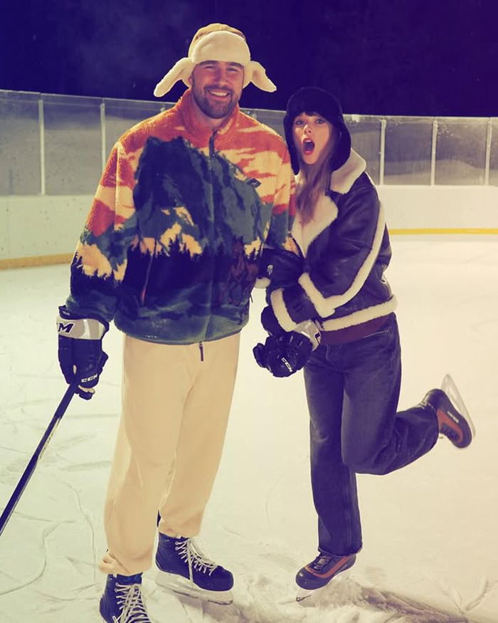 Travis Kelce and woman ice skating together at an outdoor rink during nighttime in warm winter clothing.