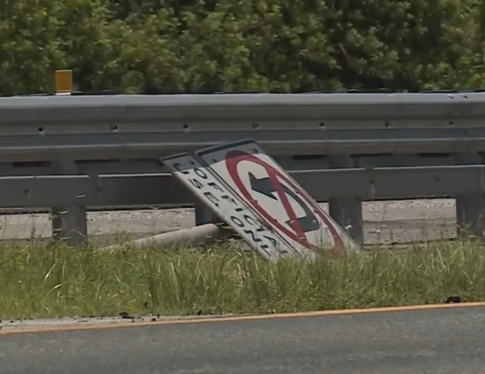 Fallen no U-turn traffic sign next to highway guardrail, relating to illegal U-turn and truck driver crash incident.