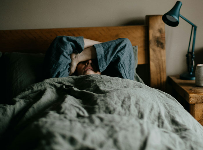Person lying in bed with arms covering face, conveying a sense of spooky and terrifying encounters that still haunt them today.