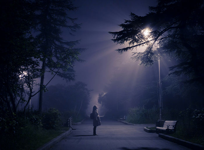 Person standing alone on a dark, foggy path under streetlights, evoking terrifying and spooky encounters at night.