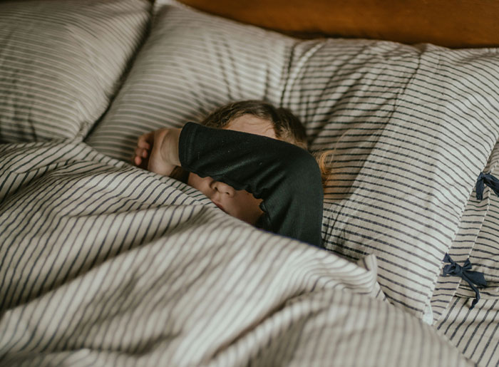 Person lying in bed covering face with arm, illustrating spooky encounters and terrifying moments that still haunt them today.