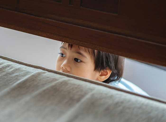 Child peeking nervously from behind a couch, capturing the feeling of a terrifying and spooky encounter that haunts today.