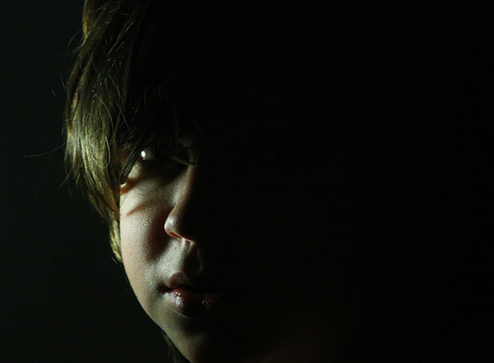 Close-up of a young person’s face half-lit in darkness, evoking a spooky and terrifying encounter atmosphere.