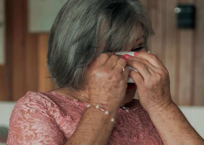Elderly woman wiping tears, illustrating emotional reactions to unhinged mother-in-law comments in a home setting.