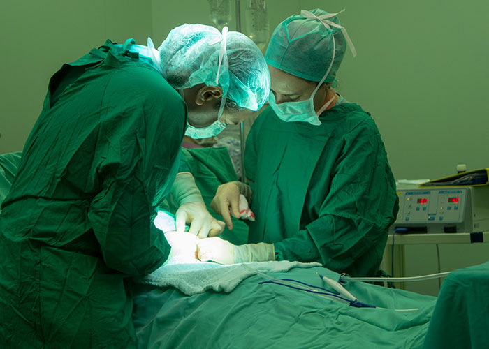 Two surgeons in green scrubs and masks performing surgery in a sterile operating room setting.