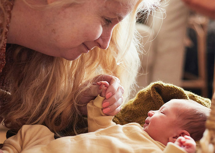 Older woman smiling and holding a newborn's hand, illustrating unhinged things MILs thought were appropriate to say out loud.