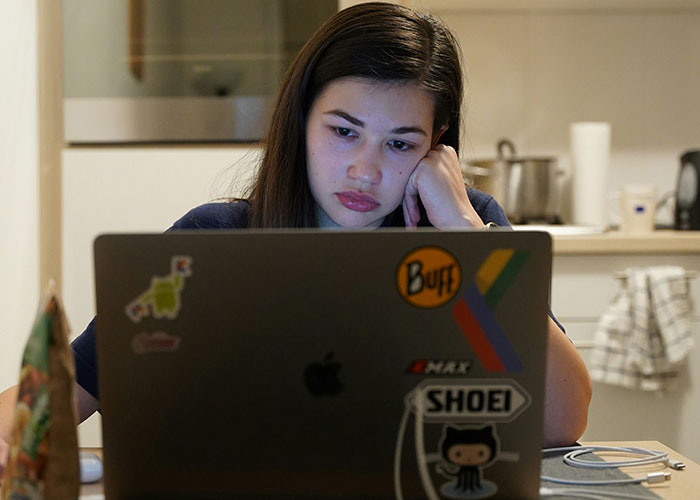 Young woman looking stressed while working on a laptop, reflecting on unhinged things MILs said out loud.