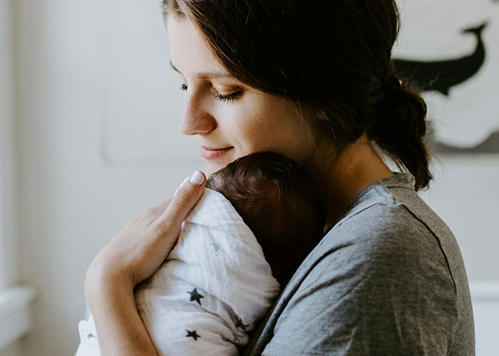 Young woman lovingly holding newborn baby wrapped in blanket, illustrating unhinged things MILs thought appropriate to say out loud