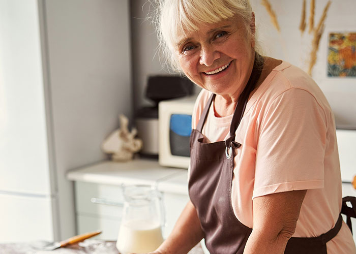 Smiling older woman in an apron standing in the kitchen, representing unhinged things MILs thought were appropriate to say.
